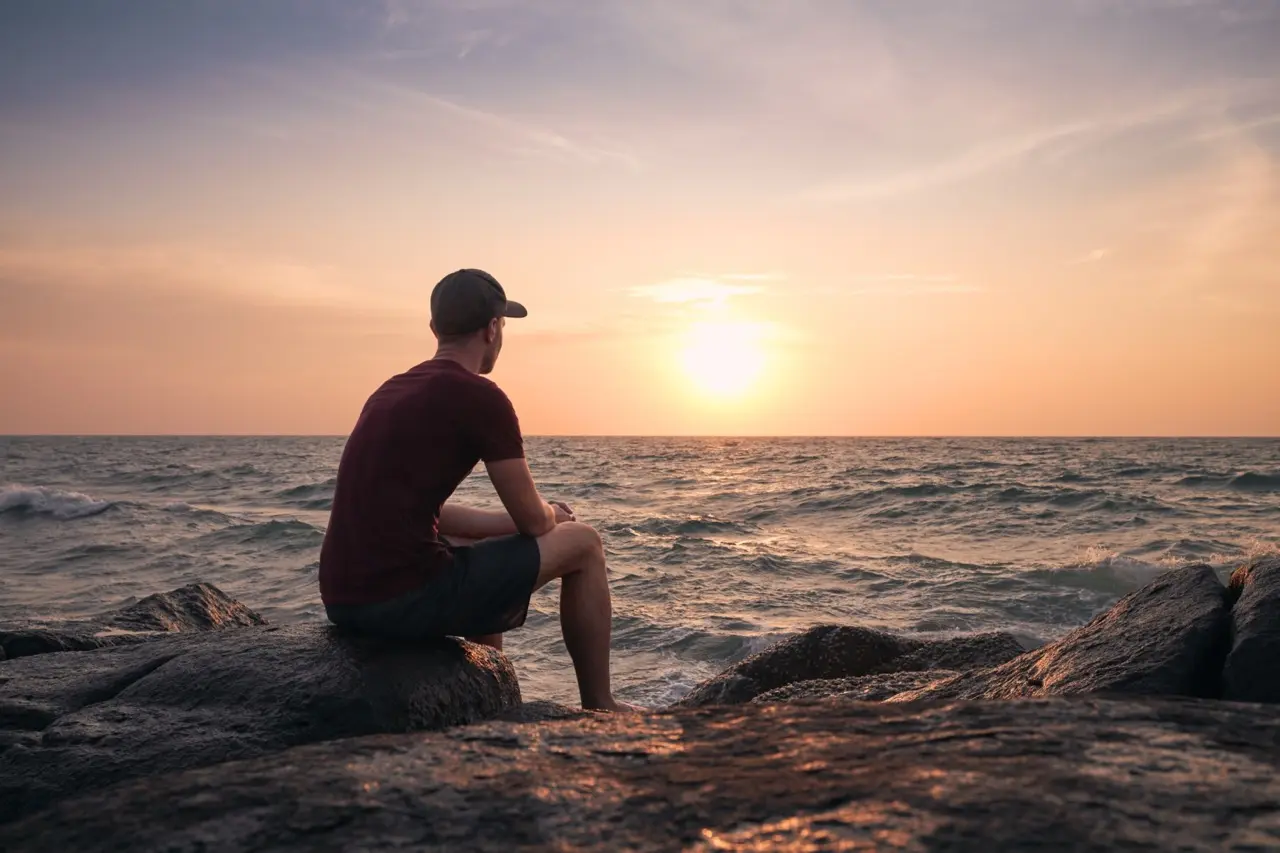 young man sitting on rocks while watching the sunset