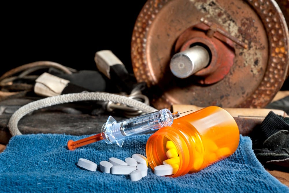 Steroid medication including pills and a syringe in front of exercise equipment. Image can be used for steroid and performance enhancement inferences in sports.