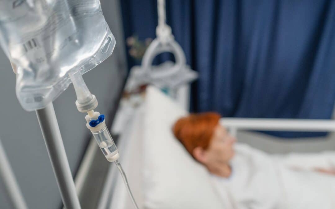Close-up of iv drip hanging above the bed with patient in the hospital ward