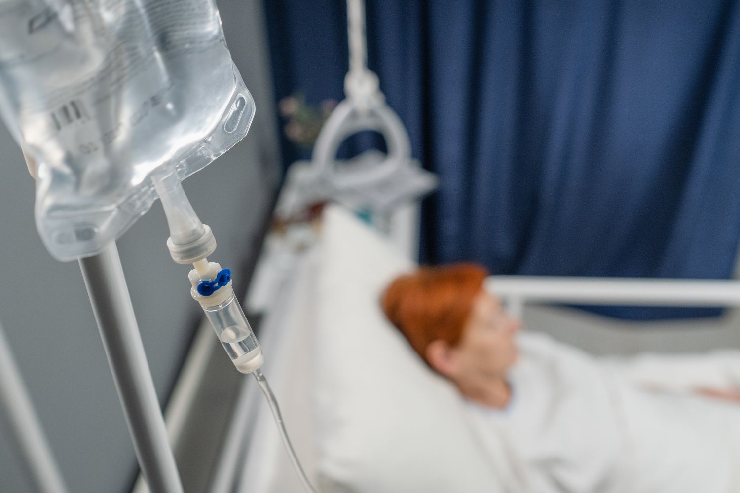 Closeup of iv drip hanging above the bed with patient in the hospital ward