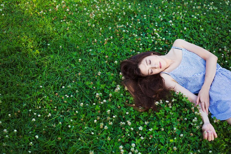 Young woman with long brown hair lying on a lawn.