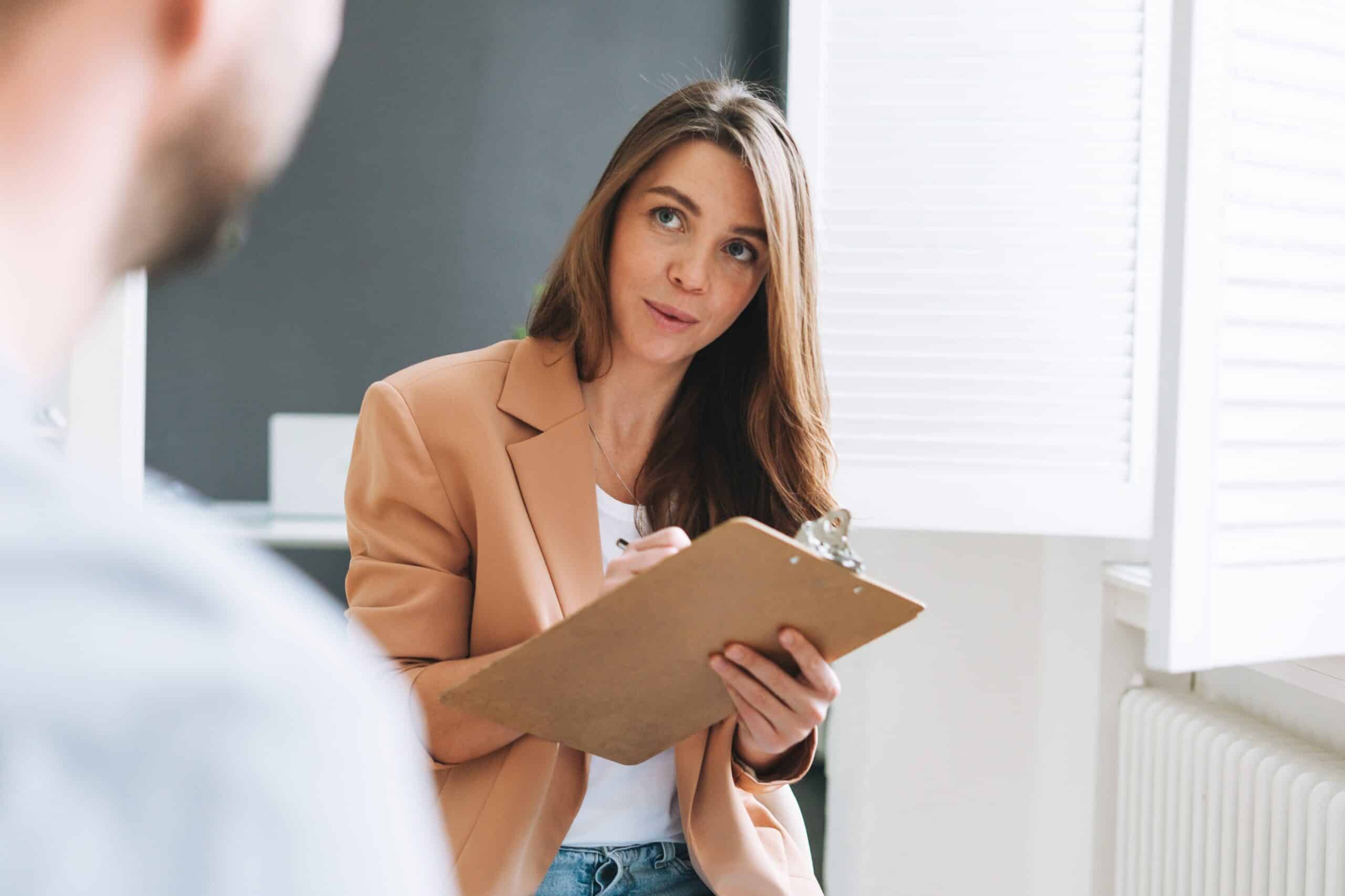 A woman listening to a man while talking while holding a clipboard and talking about insurance.