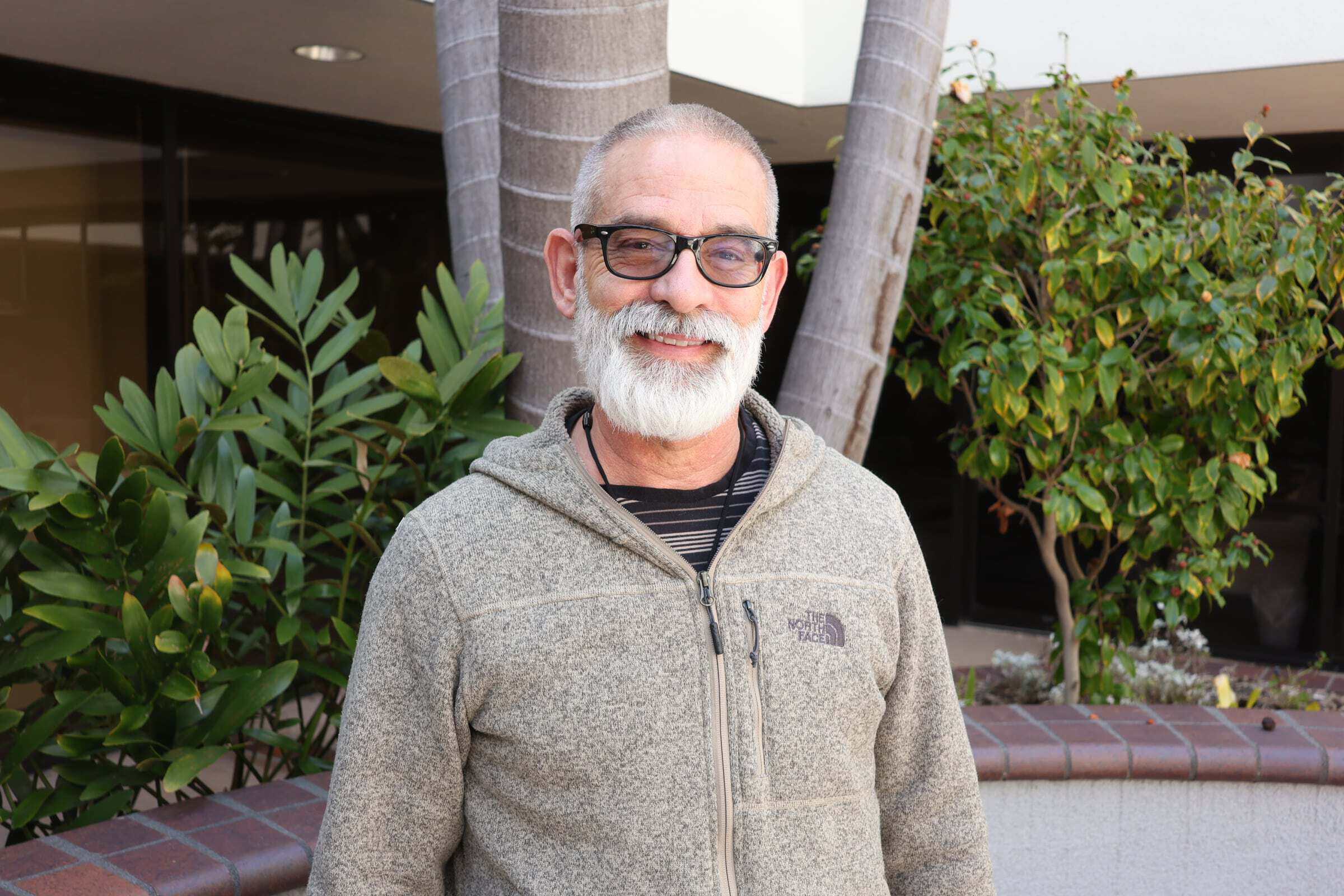 Smiling male staff member with glasses and gray beard outside.