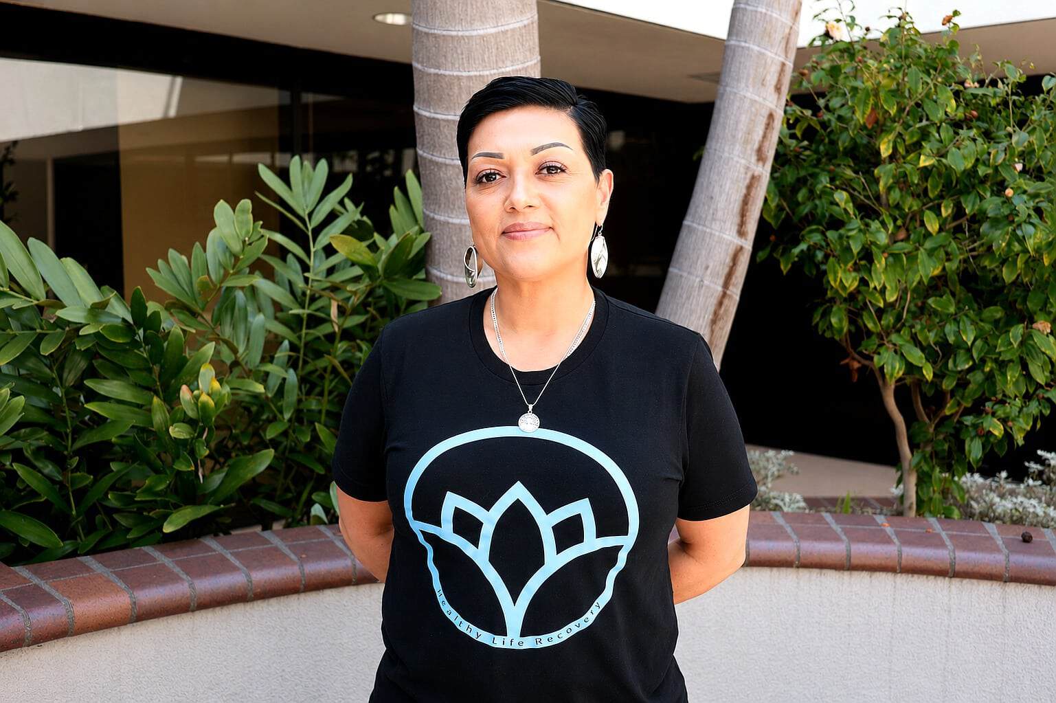 Staff member at Healthy Life Recovery standing outdoors with greenery.