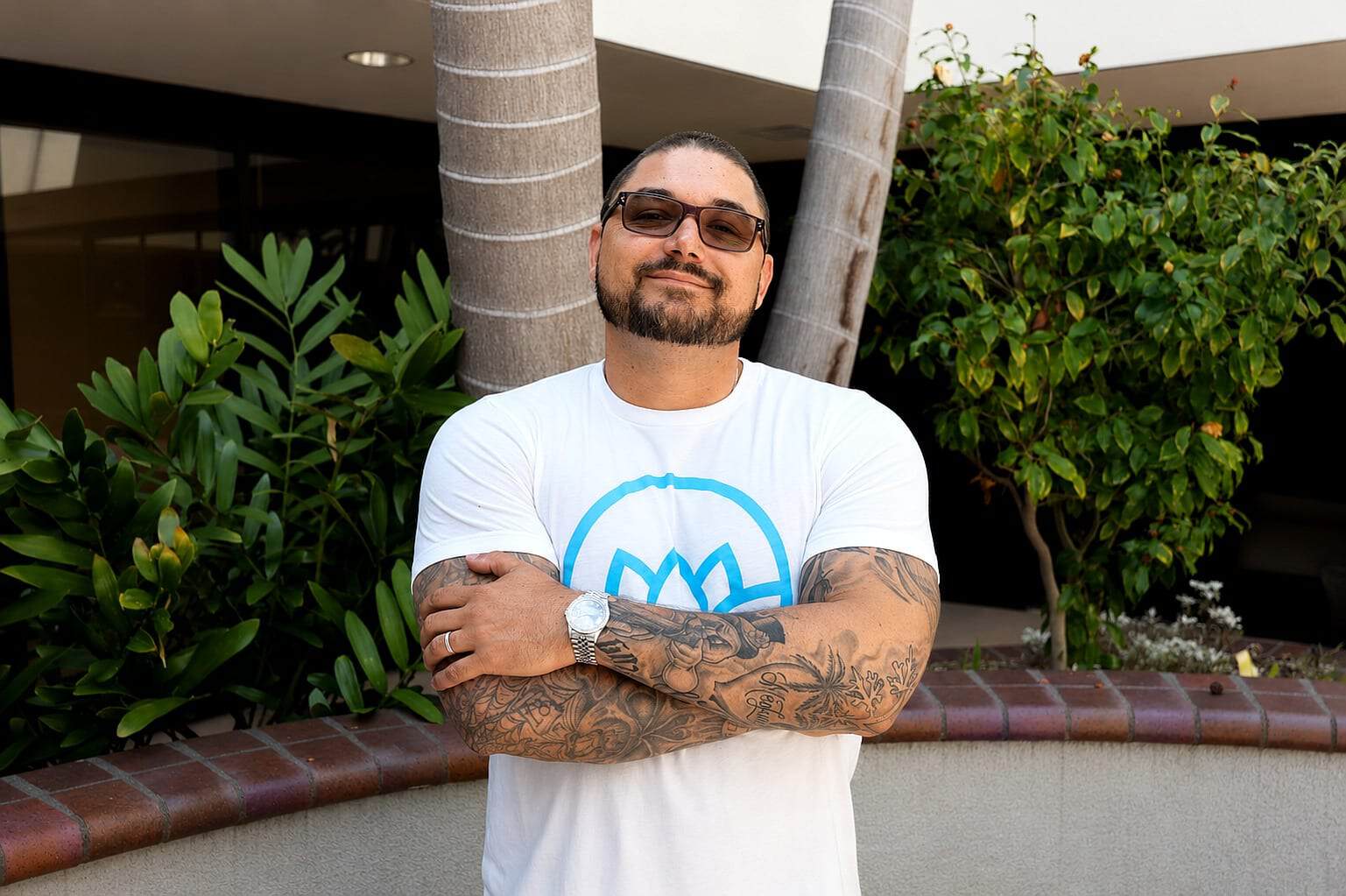 Smiling man with tattoos and sunglasses standing outdoors at Healthy Life Recovery.